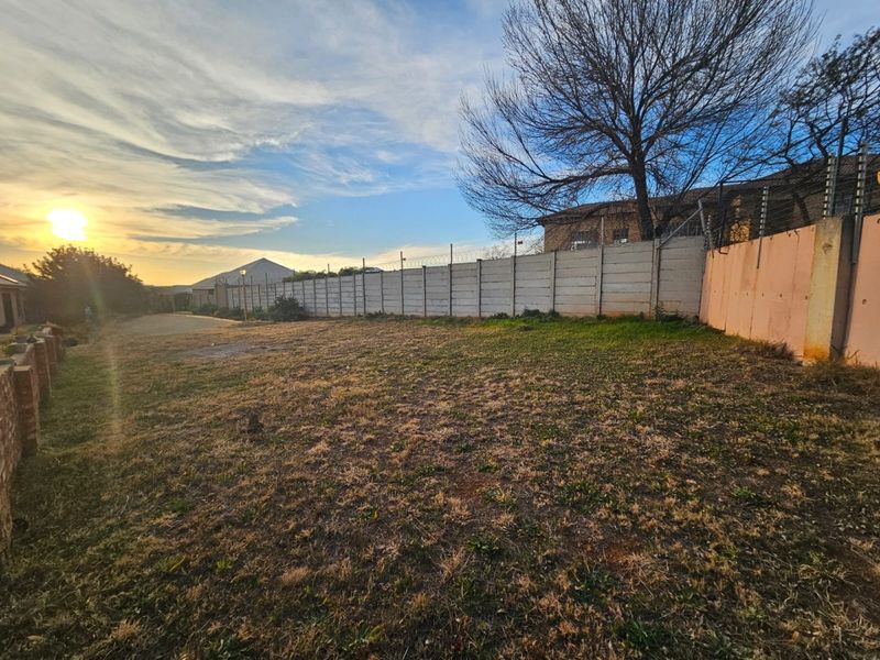 A vacant residential plot featuring a precast concrete boundary wall with electric fencing, set against a sunset backdrop.