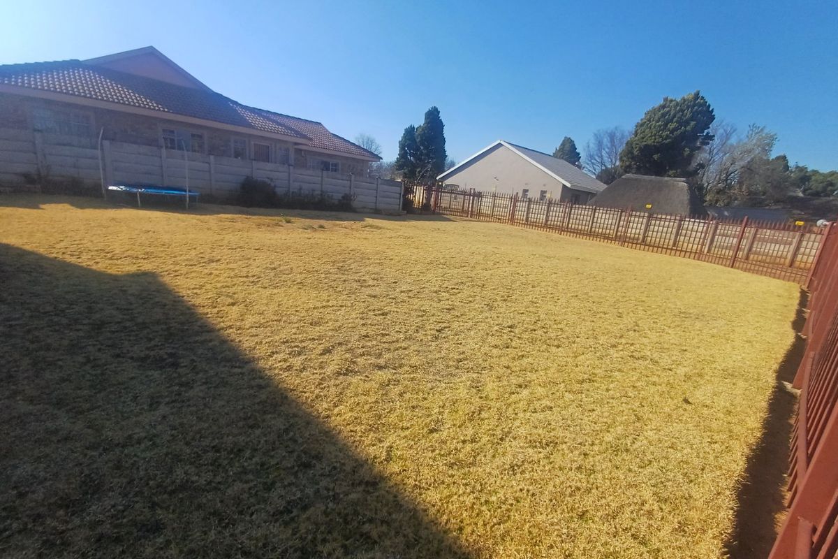 A spacious residential backyard featuring a large lawn area enclosed by precast concrete walls and metal perimeter fencing.