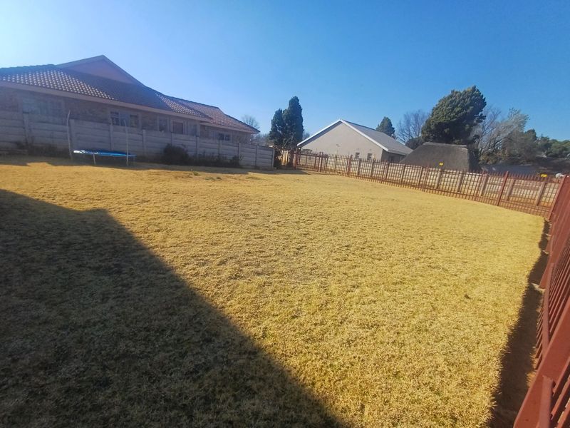 A spacious residential backyard featuring a large lawn area enclosed by precast concrete walls and metal perimeter fencing.