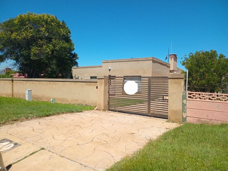 Front view of the property featuring a paved driveway, metal entrance gate, and perimeter walling with a chimney visible on the main structure.
