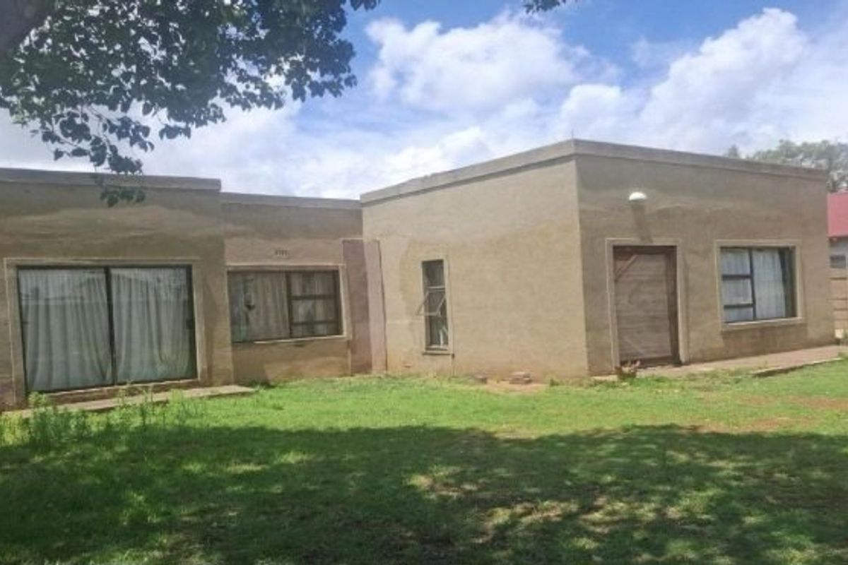 Rear view of a single-story house featuring plastered exterior walls, aluminium window frames, and sliding glass doors opening onto a garden area.