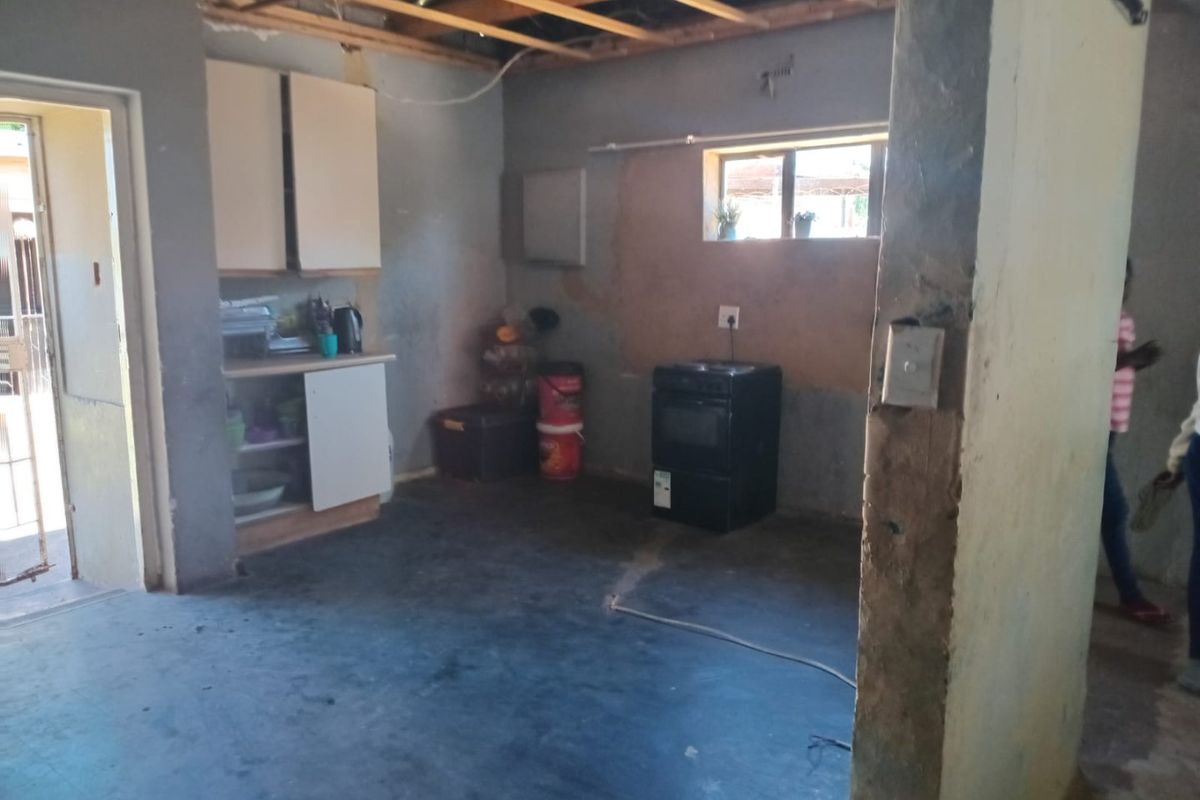 A kitchen space in need of renovation, featuring exposed ceiling joists, basic cabinetry, and unfinished wall surfaces.