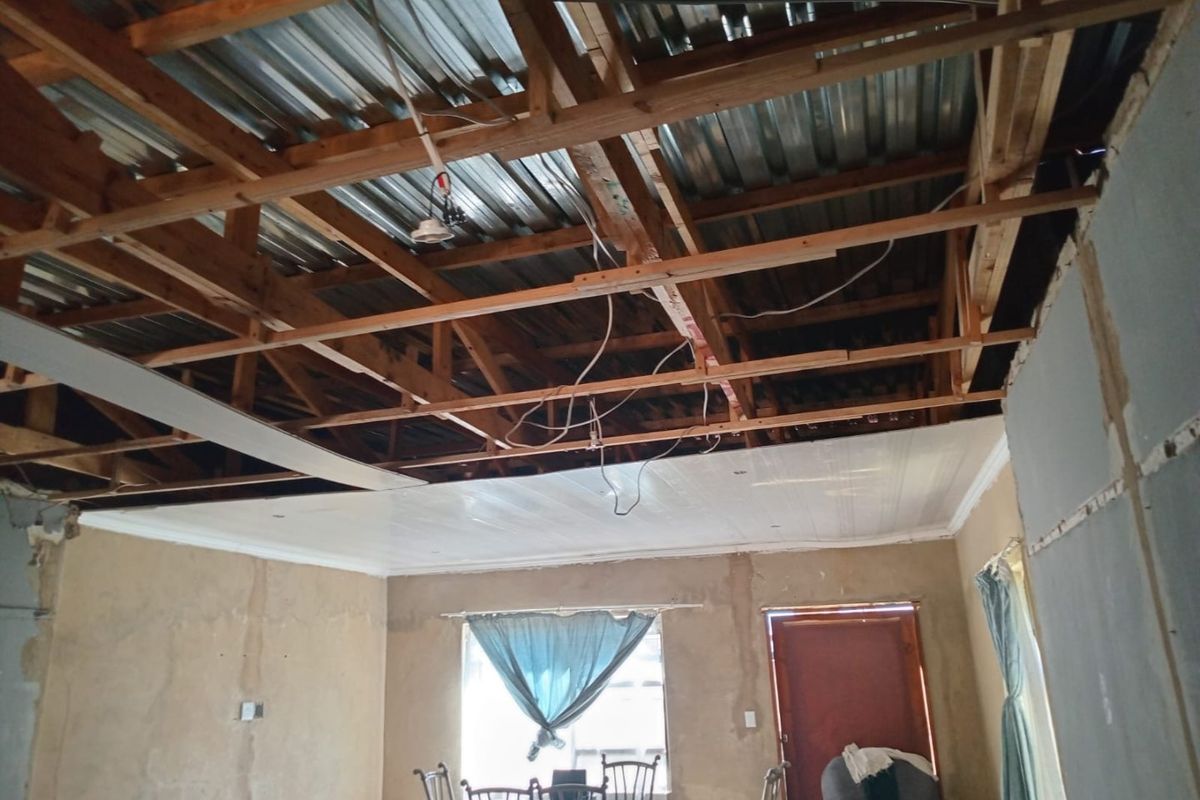 Living area currently undergoing renovation with exposed timber roof trusses, missing ceiling panels, and unfinished wall surfaces requiring completion.