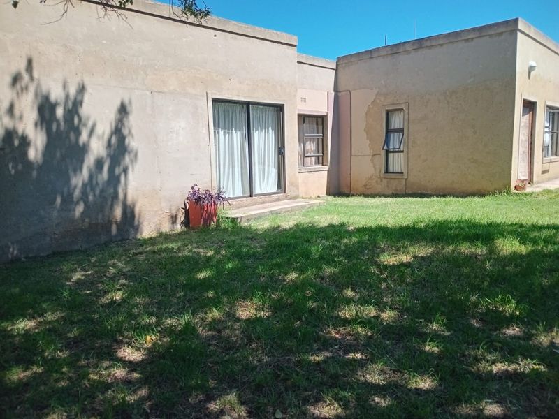 Rear view of the property showing a grass lawn, sliding glass door access, and exterior walls requiring maintenance and repainting.