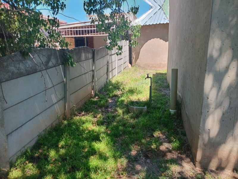 A narrow side or rear yard area featuring a precast concrete boundary wall, an external water tap, and basic drainage infrastructure.