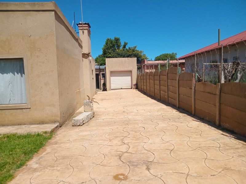 Rear exterior view featuring a paved driveway, a detached garage, and perimeter precast concrete walling.