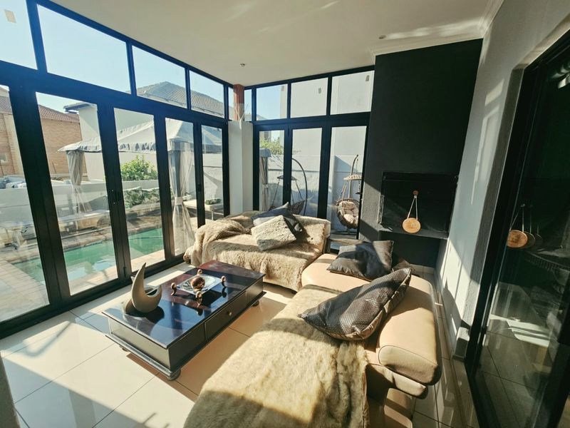 A bright, enclosed patio featuring large glass folding doors, tiled flooring, and a built-in fireplace, offering a seamless transition to the pool area.