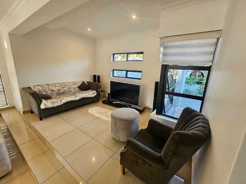 A well-maintained living room featuring neutral tiled flooring, recessed lighting, and modern aluminium-framed windows with fitted blinds.