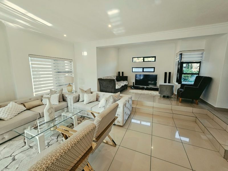Spacious living room featuring polished porcelain floor tiles, a raised platform area, and modern recessed lighting with neutral wall finishes.