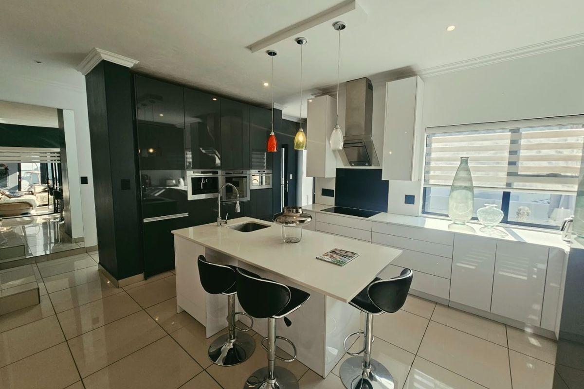 Modern kitchen featuring a central island, high-gloss cabinetry, integrated appliances, and sleek tiled flooring with contemporary pendant lighting.