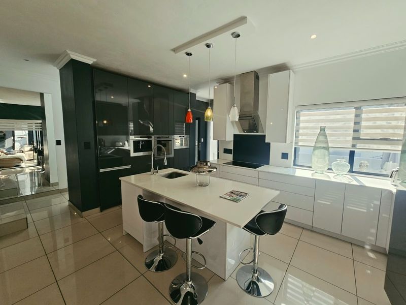 Modern kitchen featuring a central island, high-gloss cabinetry, integrated appliances, and sleek tiled flooring with contemporary pendant lighting.