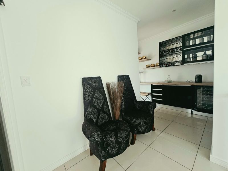 A modern home bar area featuring sleek black cabinetry, integrated wine cooling, and dedicated glassware storage with polished tiled flooring.