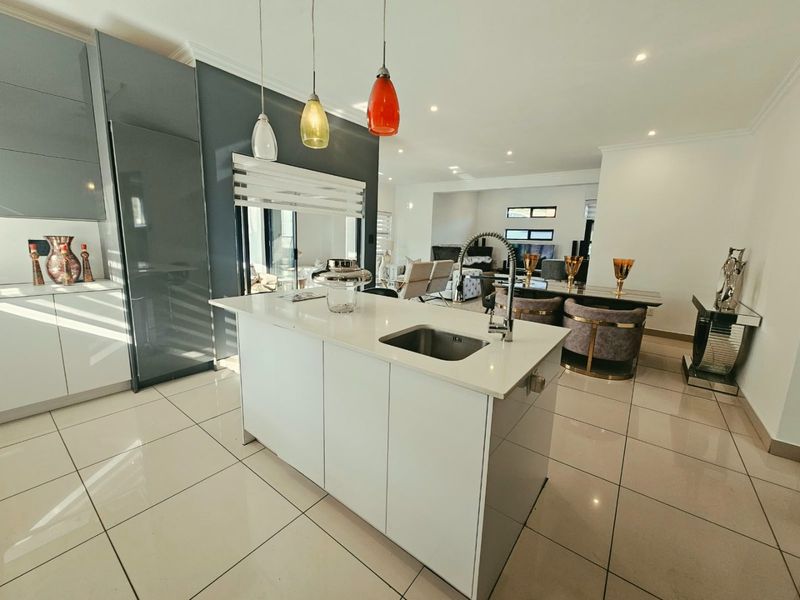 Modern open-plan kitchen featuring a central island with quartz countertops, sleek glossy cabinetry, and high-end finishes flowing into the dining and living areas.