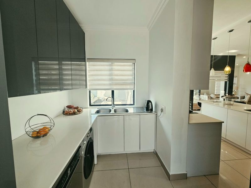 A modern scullery featuring sleek high-gloss cabinetry, a double sink, and tiled flooring, providing a functional and organized secondary kitchen prep area.
