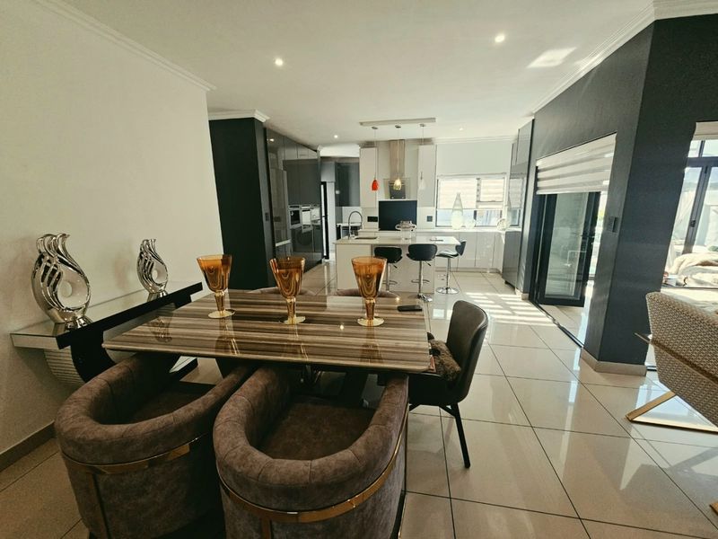 Modern open-plan living and dining area featuring a sleek kitchen with a central island, high-gloss cabinetry, and seamless access to the outdoor space.