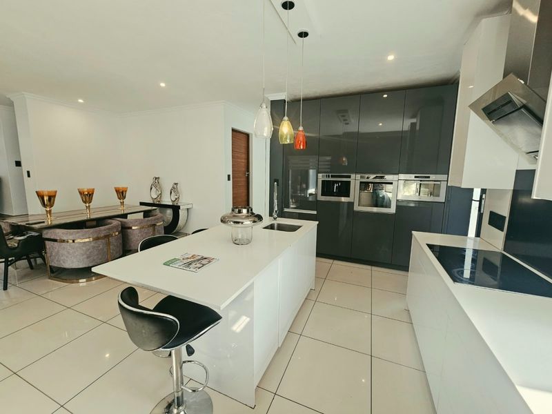 Modern open-plan kitchen and dining area featuring high-gloss cabinetry, a central island with sink, integrated appliances, and polished floor tiles.