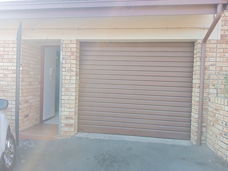 Exterior view of a single garage featuring a brown roller door and adjacent pedestrian entrance with intercom system.