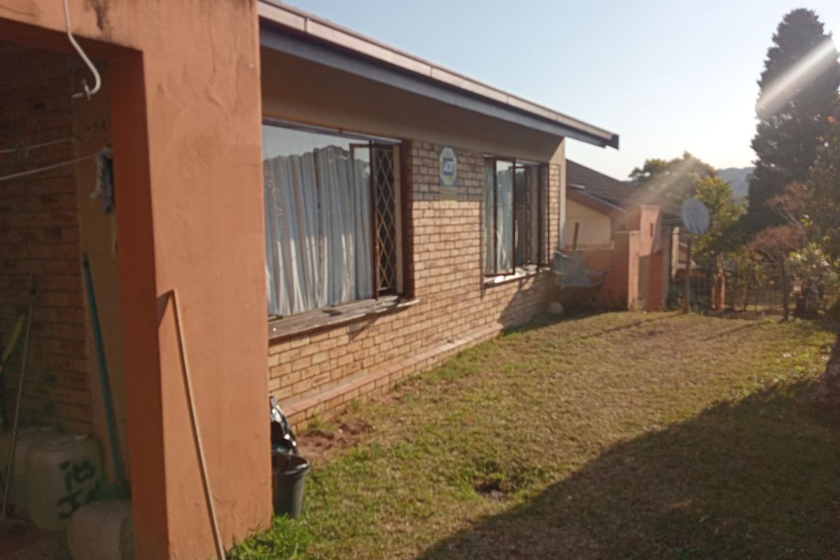 Rear view of the apartment featuring a brick facade, security bars on windows, and a covered patio area overlooking the lawn.