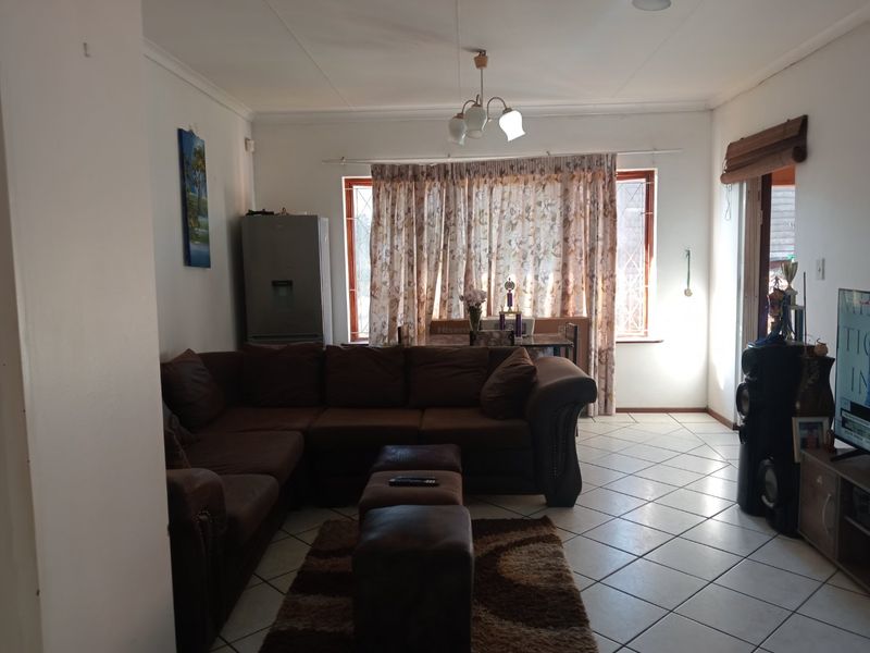 A living room featuring tiled flooring, a central ceiling light fixture, and a window fitted with security bars.
