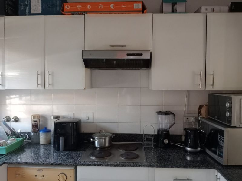 A functional kitchen featuring white cabinetry, a granite countertop, tiled backsplash, and a built-in electric hob with an overhead extractor fan.