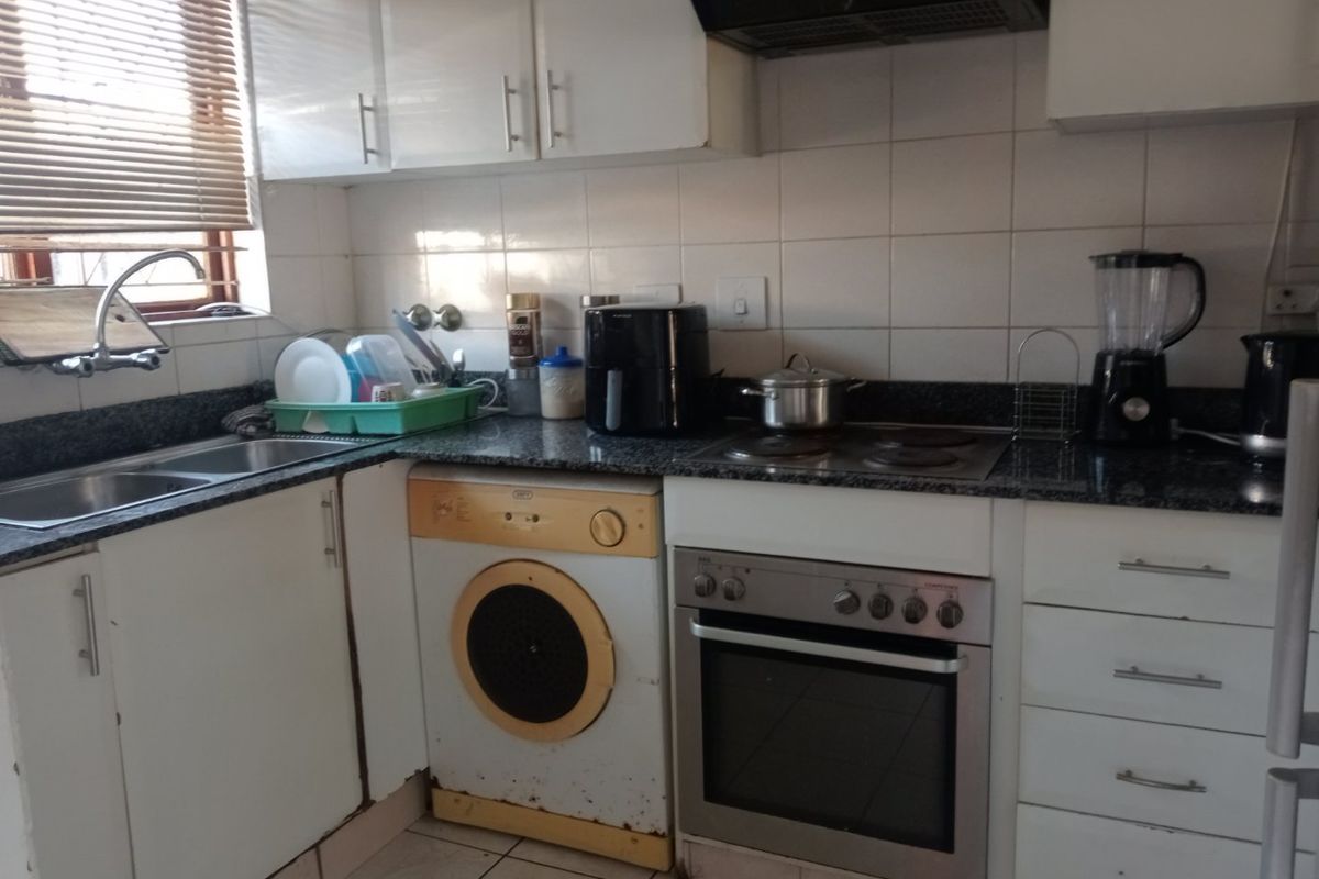 Compact kitchen featuring granite countertops, built-in oven, electric hob, extractor fan, and white cabinetry with tiled backsplash and flooring.