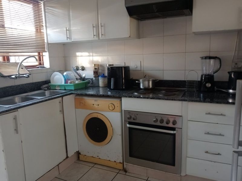 Compact kitchen featuring granite countertops, built-in oven, electric hob, extractor fan, and white cabinetry with tiled backsplash and flooring.