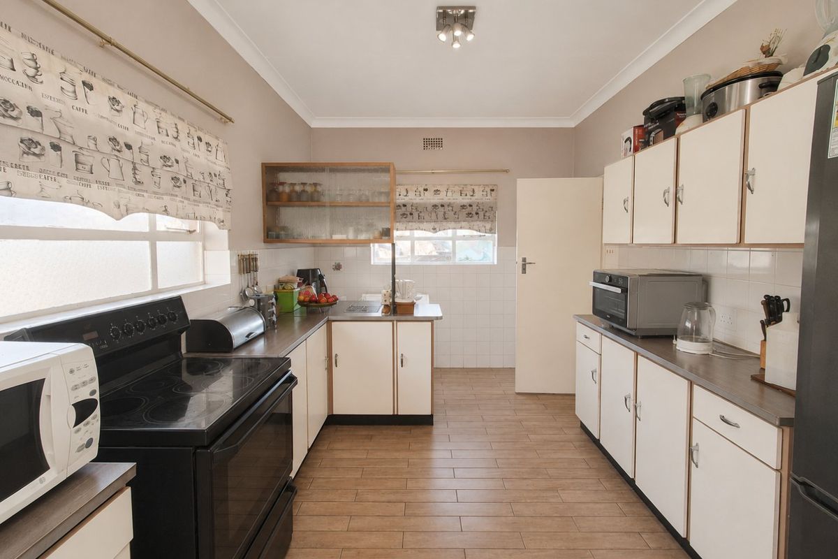 A functional kitchen featuring white cabinetry, tiled backsplash, laminate countertops, and wood-look ceramic floor tiles with ample storage space.