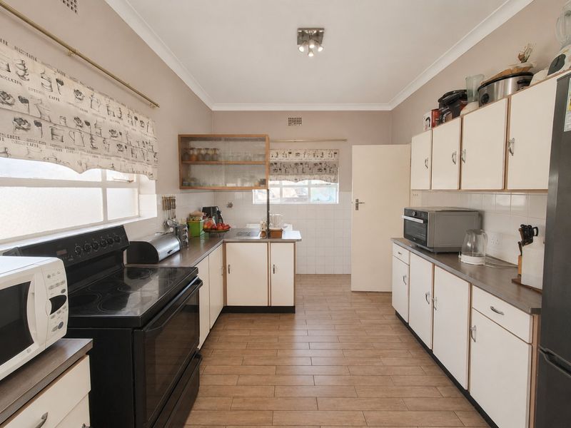 A functional kitchen featuring white cabinetry, tiled backsplash, laminate countertops, and wood-look ceramic floor tiles with ample storage space.