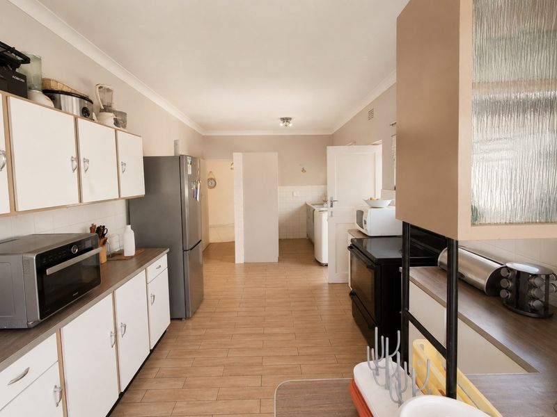 A functional kitchen featuring white cabinetry, wood-look tiled flooring, and a tiled backsplash, offering a practical layout with ample storage and workspace.