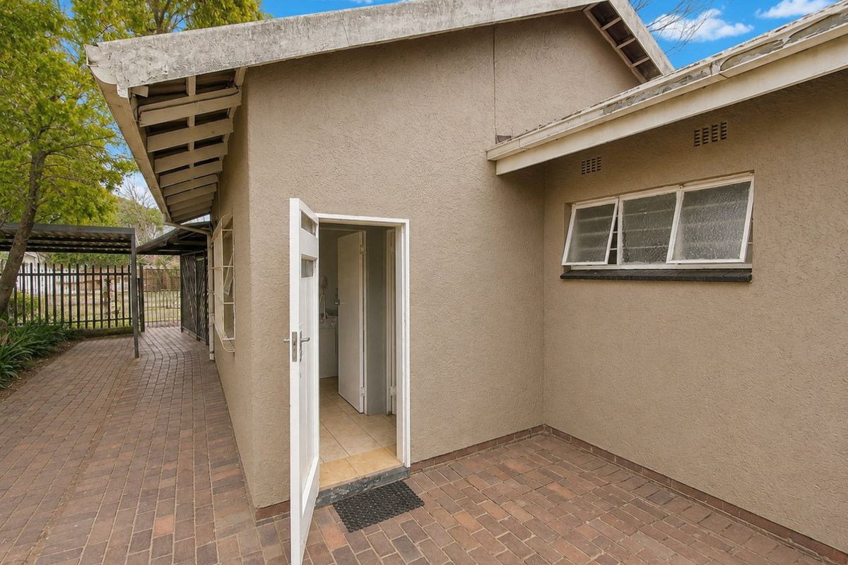 Rear exterior view of the property featuring a paved patio area, brick paving, and access to the interior through a side door.