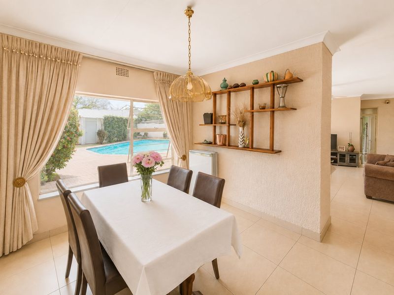 Bright dining area featuring tiled floors, built-in wall shelving, and a large window with views overlooking the outdoor pool area.