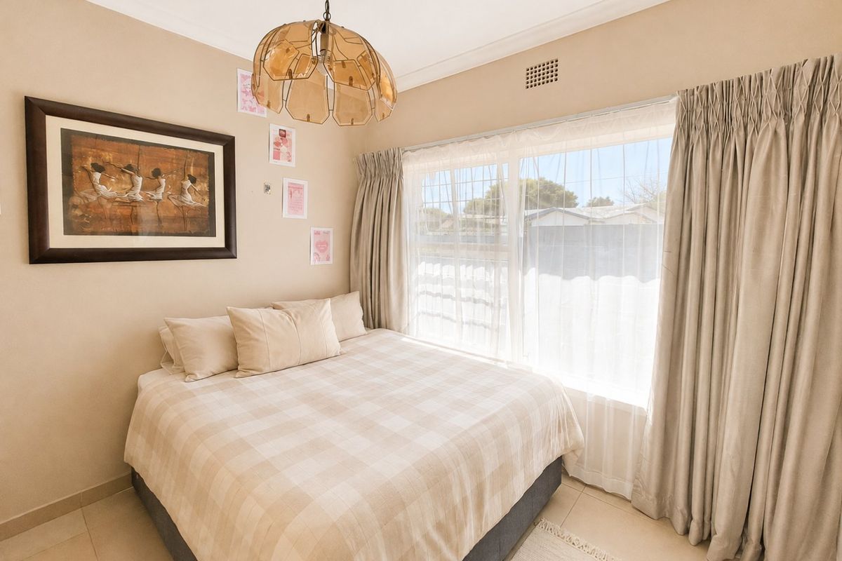 A neutrally decorated bedroom featuring tiled flooring, a large window with curtains, and a central pendant light fixture.