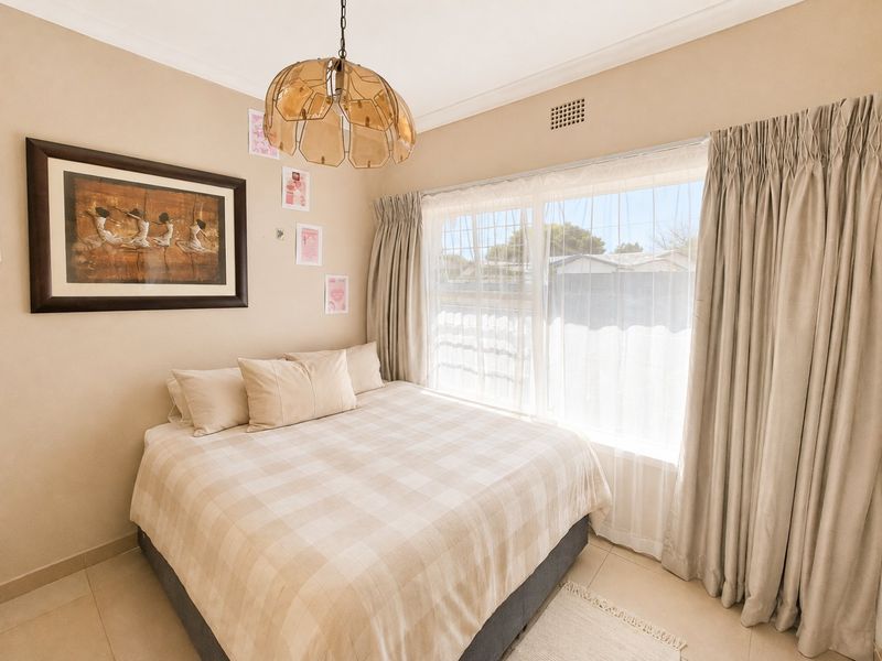 A neutrally decorated bedroom featuring tiled flooring, a large window with curtains, and a central pendant light fixture.