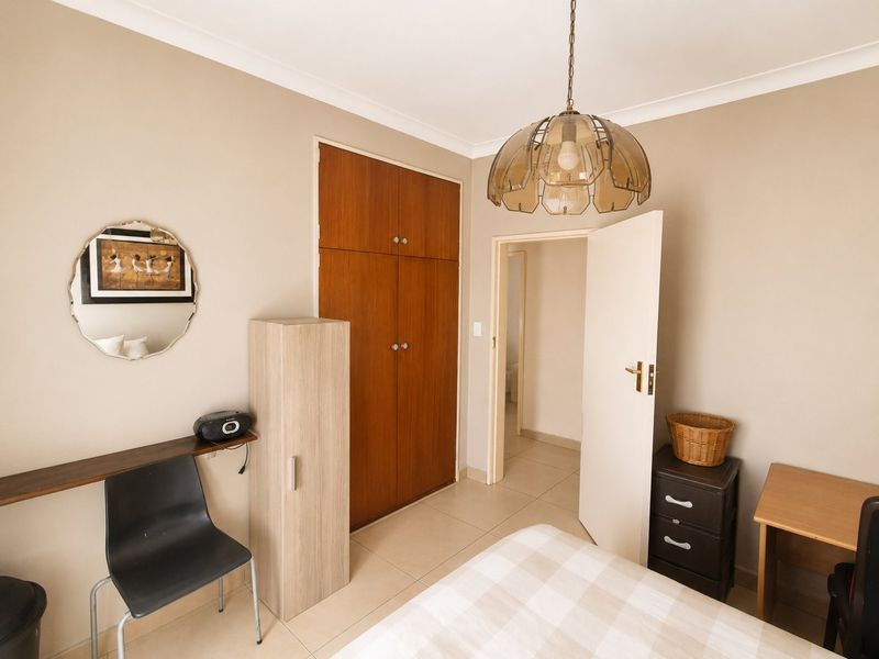 A bedroom featuring tiled flooring, built-in wooden cupboards, and a central pendant light fixture.