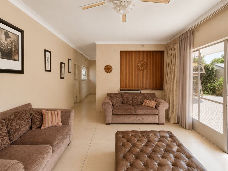 A spacious living room featuring neutral tiled flooring, a ceiling fan, and a sliding glass door providing direct access to the outdoor patio area.