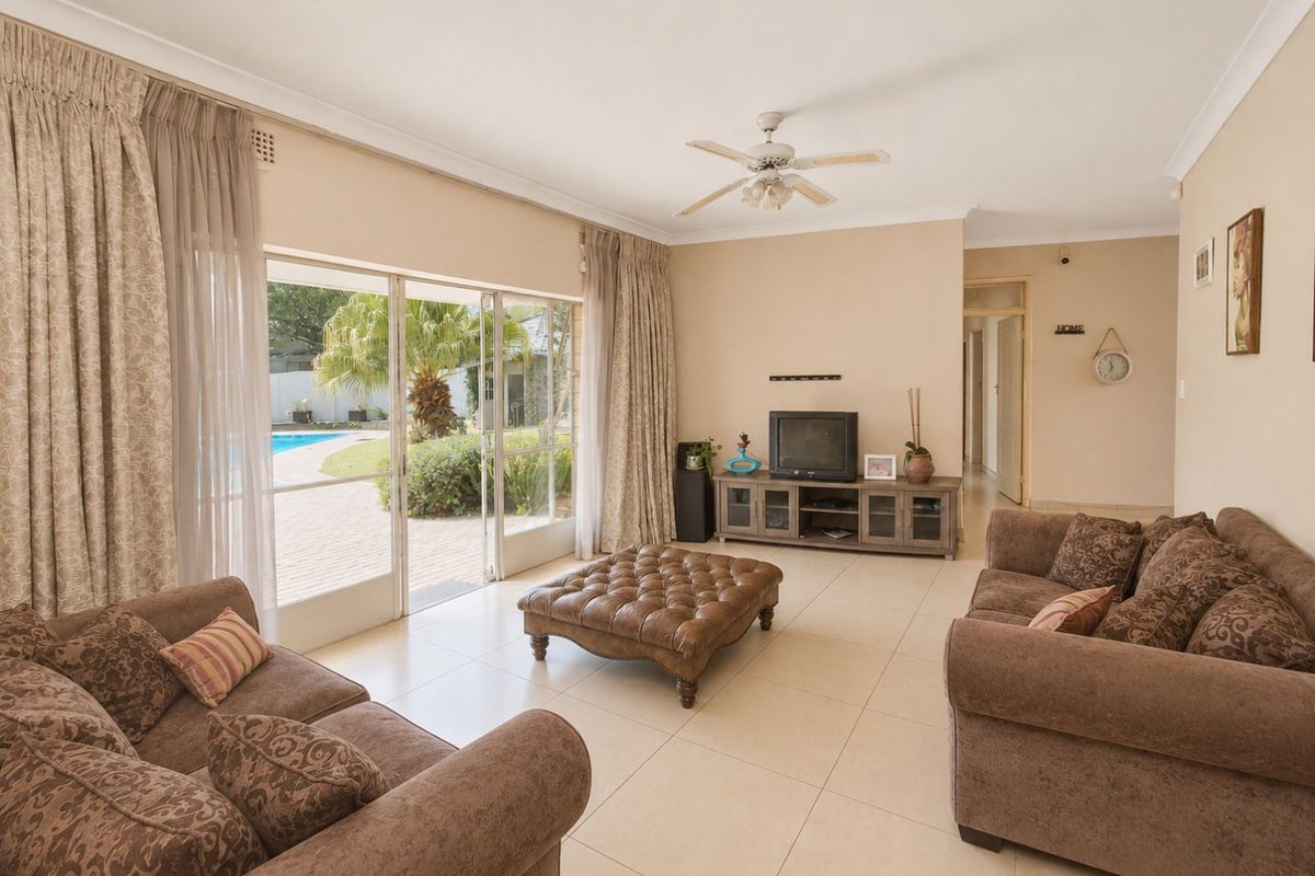 Spacious living room featuring neutral tiled flooring, a ceiling fan, and large sliding glass doors providing direct access to the outdoor pool area.