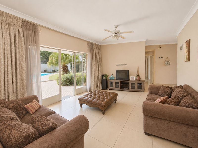 Spacious living room featuring neutral tiled flooring, a ceiling fan, and large sliding glass doors providing direct access to the outdoor pool area.