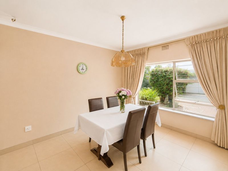 A bright dining room featuring neutral tiled flooring, cove cornicing, and a large window overlooking the garden.