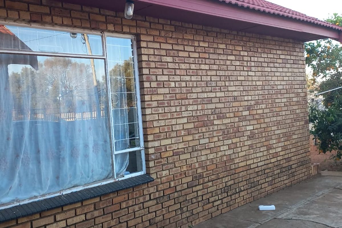 A view of the rear exterior featuring face brick walls, security bars on the windows, and a paved outdoor area.