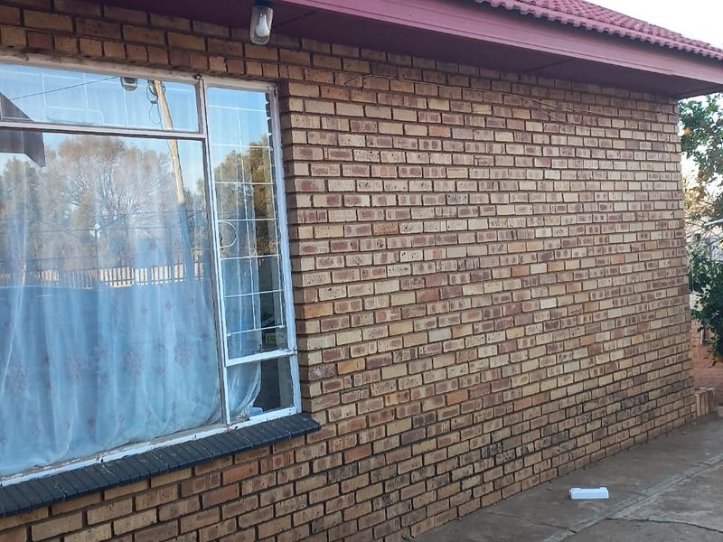 A view of the rear exterior featuring face brick walls, security bars on the windows, and a paved outdoor area.