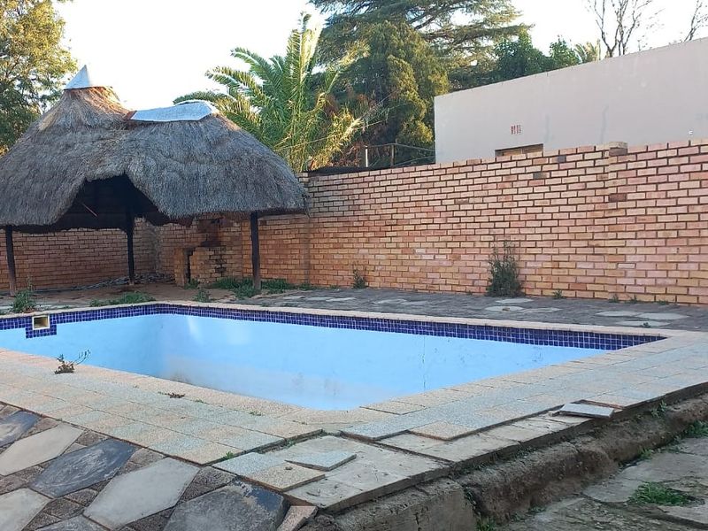 Outdoor pool area featuring a swimming pool, a thatch lapa, and brick boundary walls, requiring maintenance and repair to the paving and pool structure.