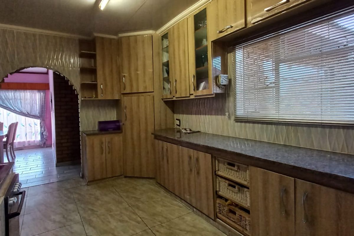 A functional kitchen featuring wood-look laminate cabinetry, ample countertop space, built-in oven, extractor fan, and tiled flooring, with an arched opening to the dining area.