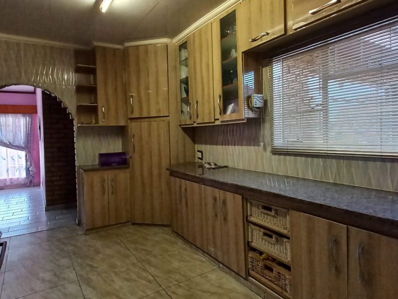 A functional kitchen featuring wood-look laminate cabinetry, ample countertop space, built-in oven, extractor fan, and tiled flooring, with an arched opening to the dining area.