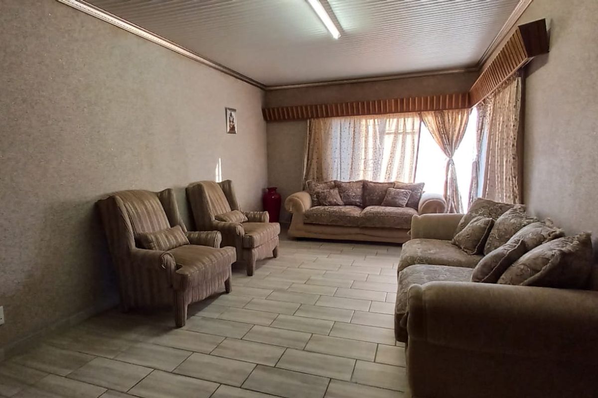 A spacious living room featuring tiled flooring, textured wall finishes, and a coved ceiling with a window pelmet.