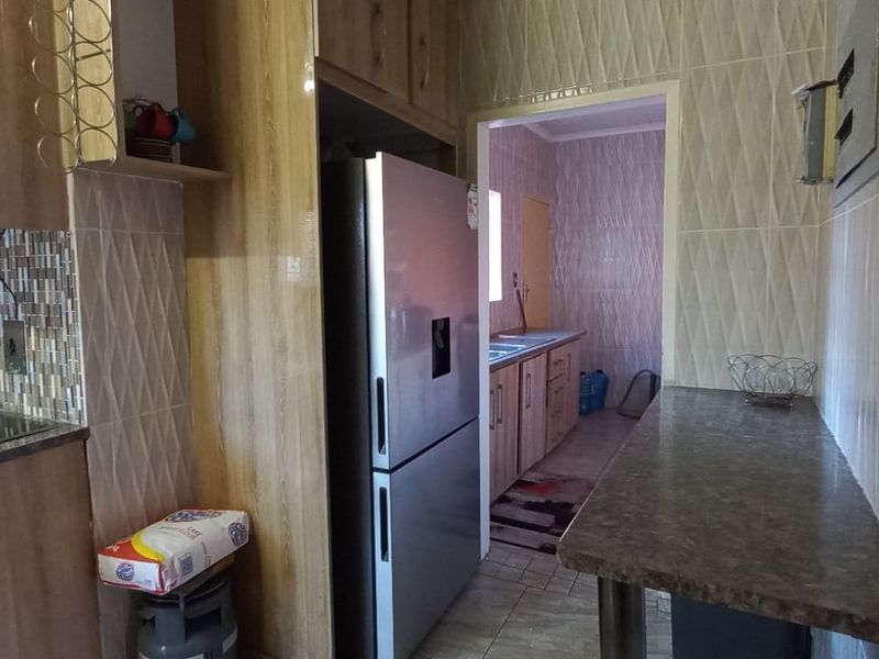 A functional kitchen featuring wood-look cabinetry, laminate countertops, built-in oven, and extractor fan, with an adjacent scullery area visible through the doorway.