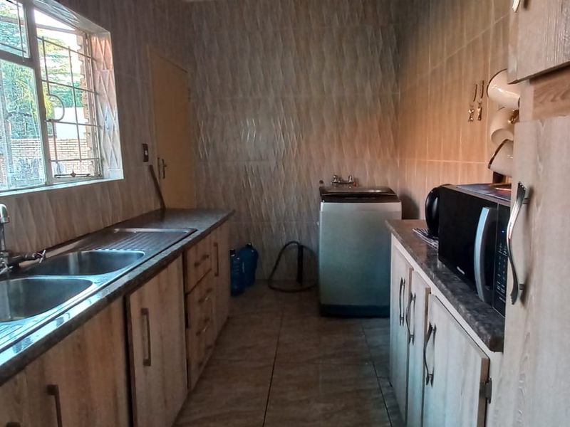 A functional scullery area featuring laminate cabinetry, a double stainless steel sink, and tiled finishes, providing additional workspace and utility storage.