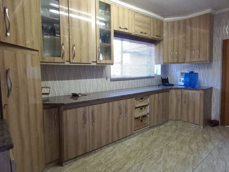 A functional kitchen featuring wood-look laminate cabinetry, granite countertops, tiled backsplash, and ceramic floor tiles with an integrated extractor fan.