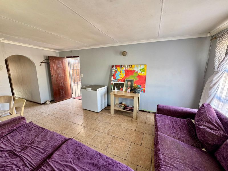 A living room featuring tiled flooring, an arched entryway, and a timber door leading to an exterior security gate.