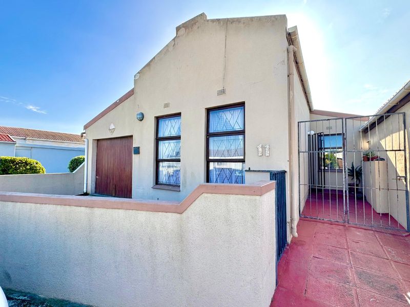 Front elevation of the property featuring a garage, secure gated entrance, and paved walkway with boundary walling.