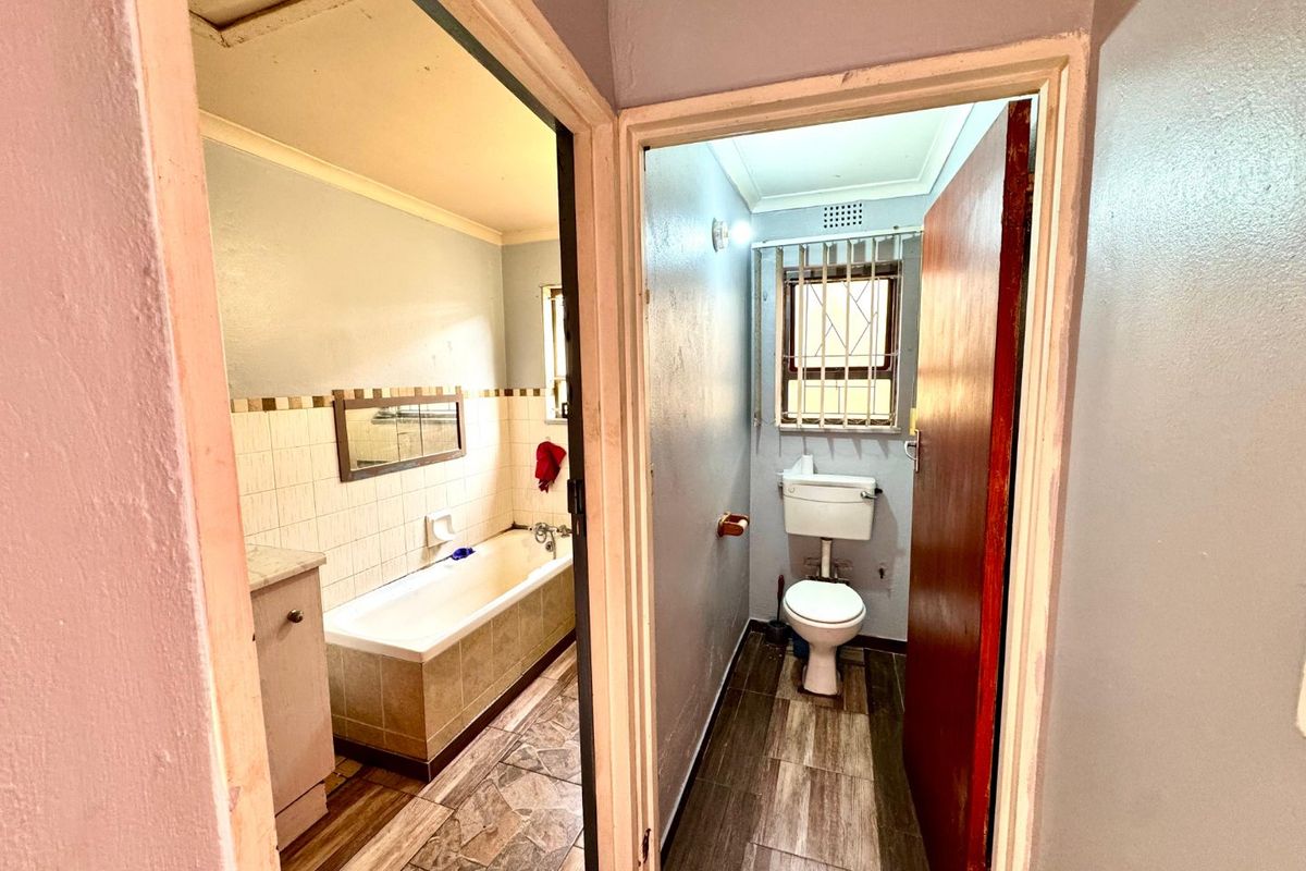 A functional bathroom featuring a built-in bathtub, vanity cabinet, and separate toilet area with tiled flooring and security window bars.